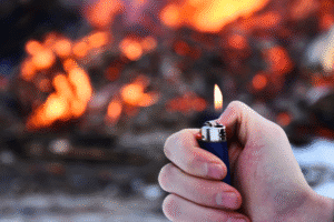 Hand holding lighter near fire – Arizona arson criminal defense concept