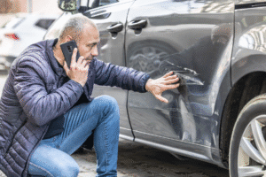 Man inspecting damage on a car after a company vehicle accident while talking on the phone