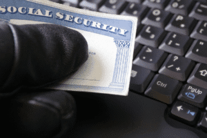 Gloved hand holding Social Security card over computer keyboard representing stolen identity in Arizona
