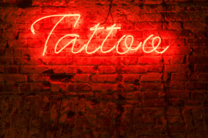 Red neon tattoo sign glowing on a brick wall at an Arizona tattoo parlor